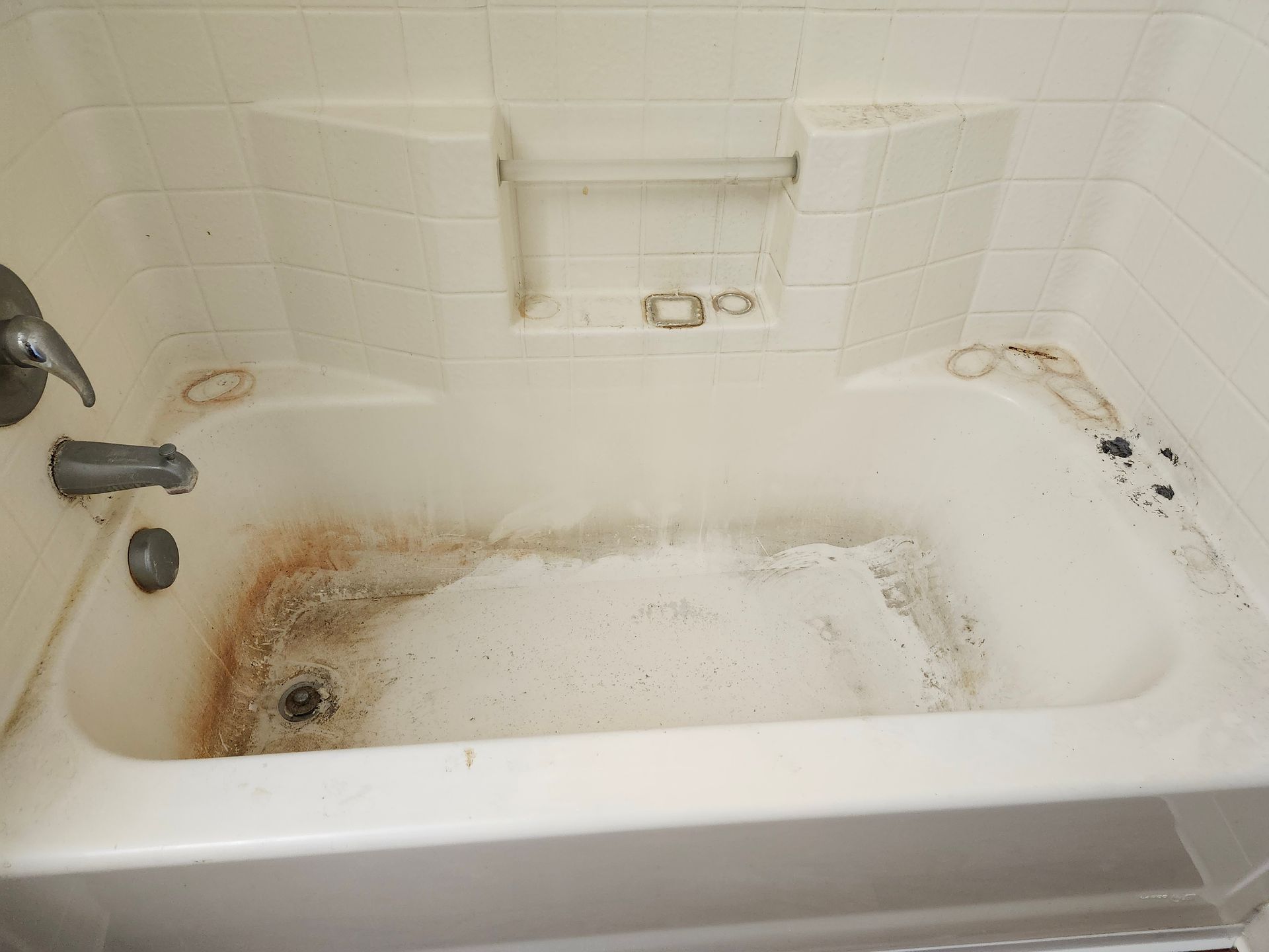 Dirty, stained white bathtub with soap scum and brown rust stains. Built-in soap holder, faucet visible.