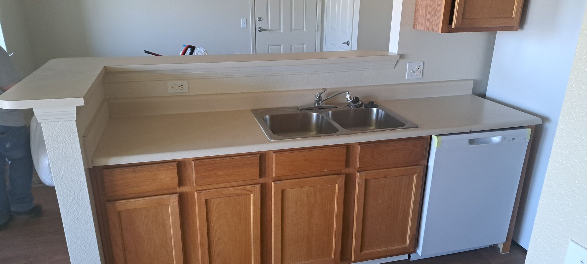 Kitchen countertop with a double sink and faucet. Beige countertop, wooden cabinets.