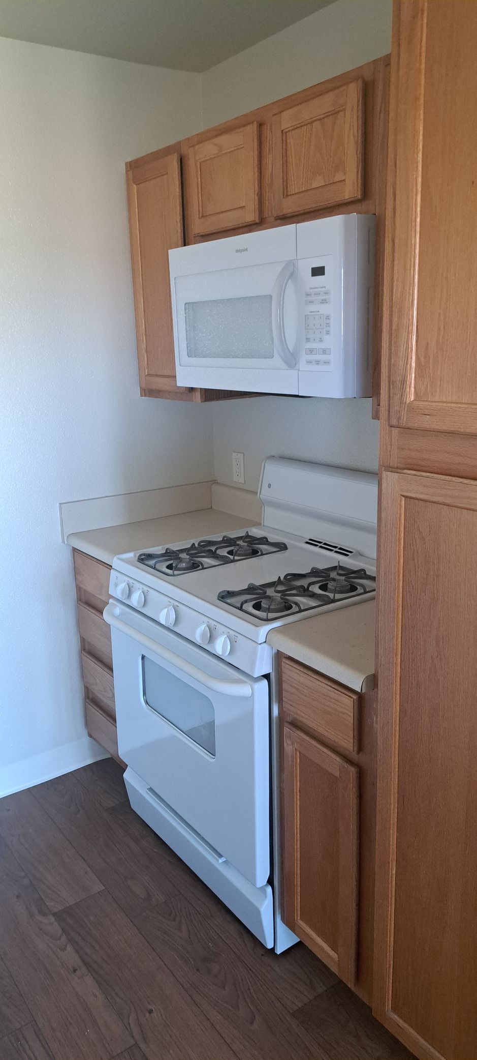 Kitchen with white appliances, light brown cabinets, and dark brown flooring.