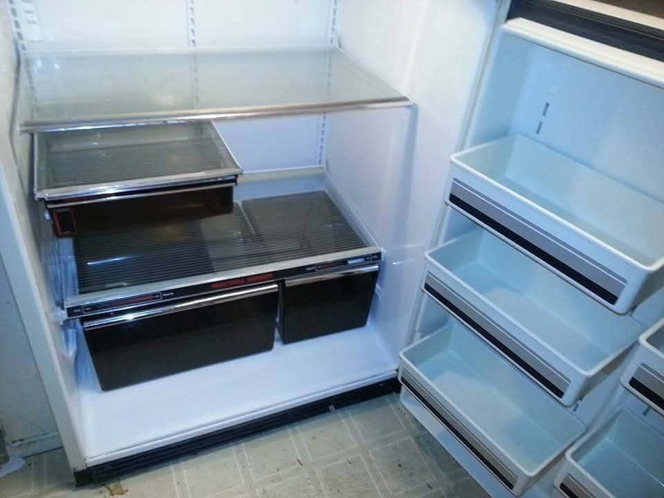 Open refrigerator interior, white shelves, black drawers, and light blue bins.