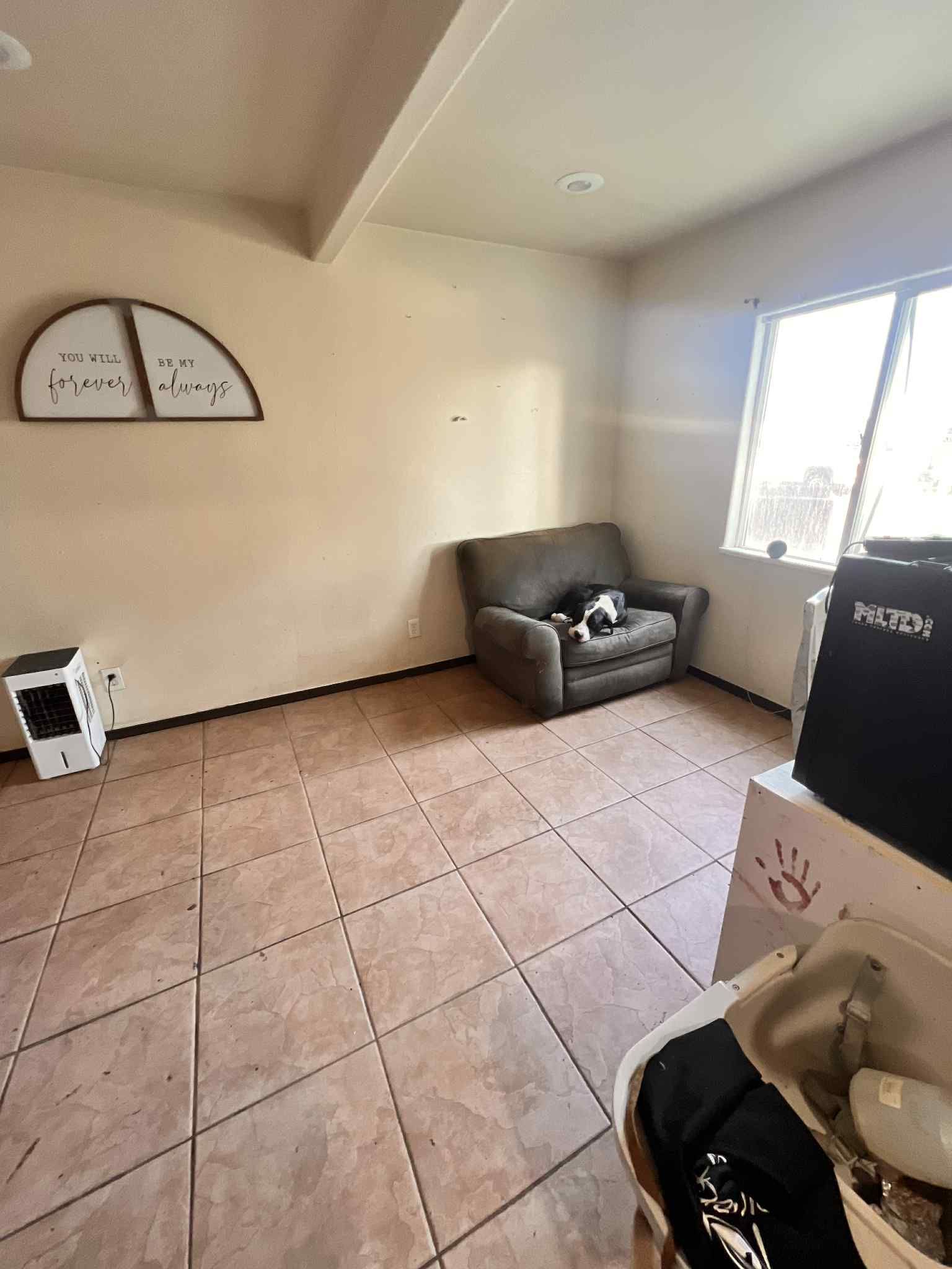 A room with tiled floor, armchair, window, a small heater, and a decorative wooden arc.