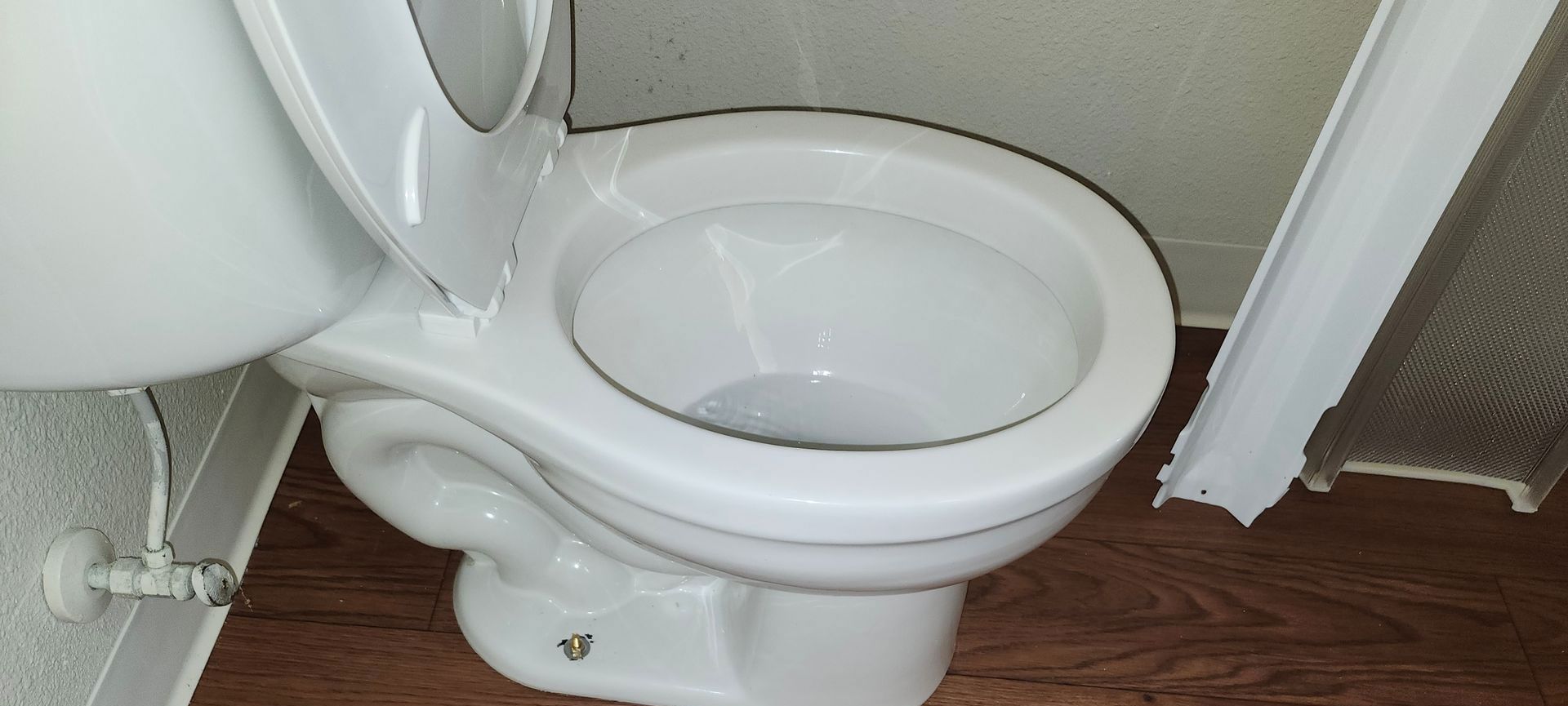 White toilet with the lid up, set against a wooden floor.