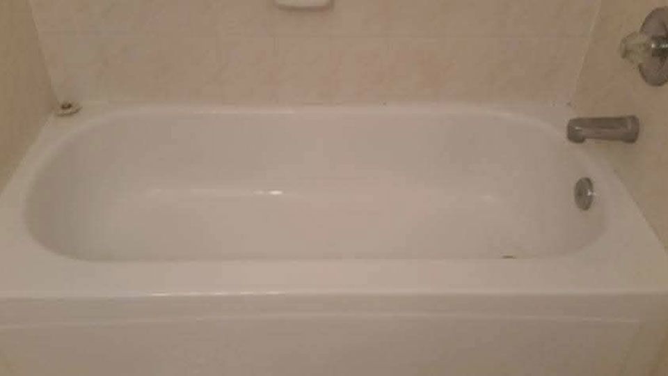 White bathtub in a bathroom with beige tile walls. Soap dish and faucet visible.