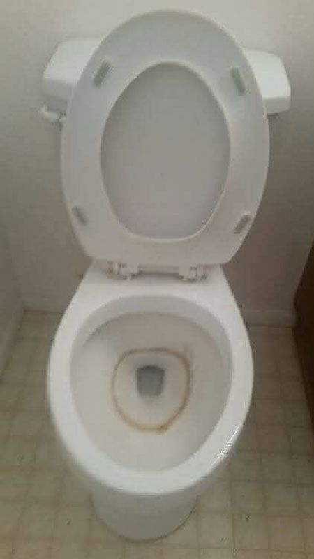 White toilet with the seat up, set on beige tile floor.