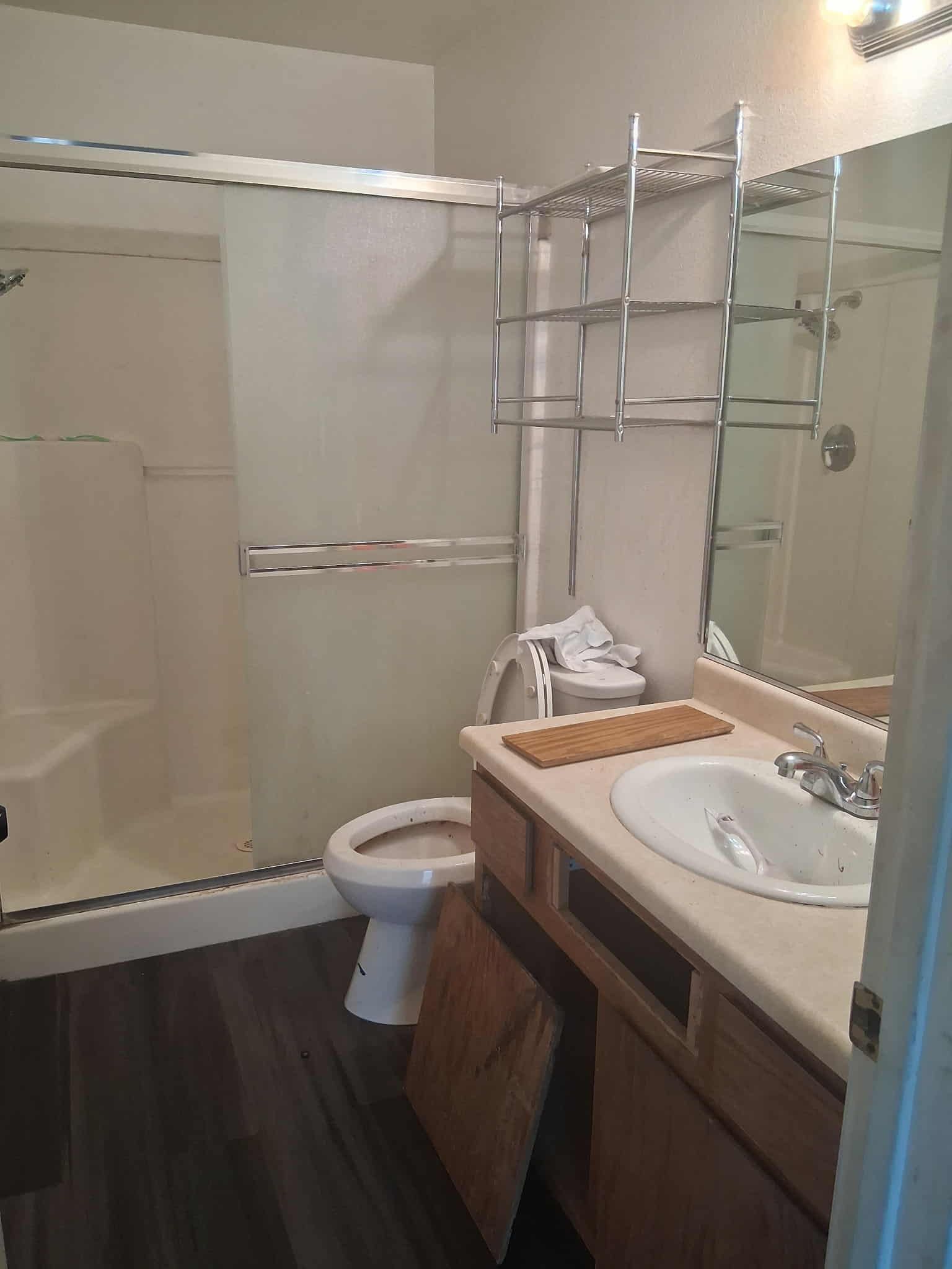 Dirty bathroom with a shower, toilet, sink, and cabinet. Dark wood-look floor.