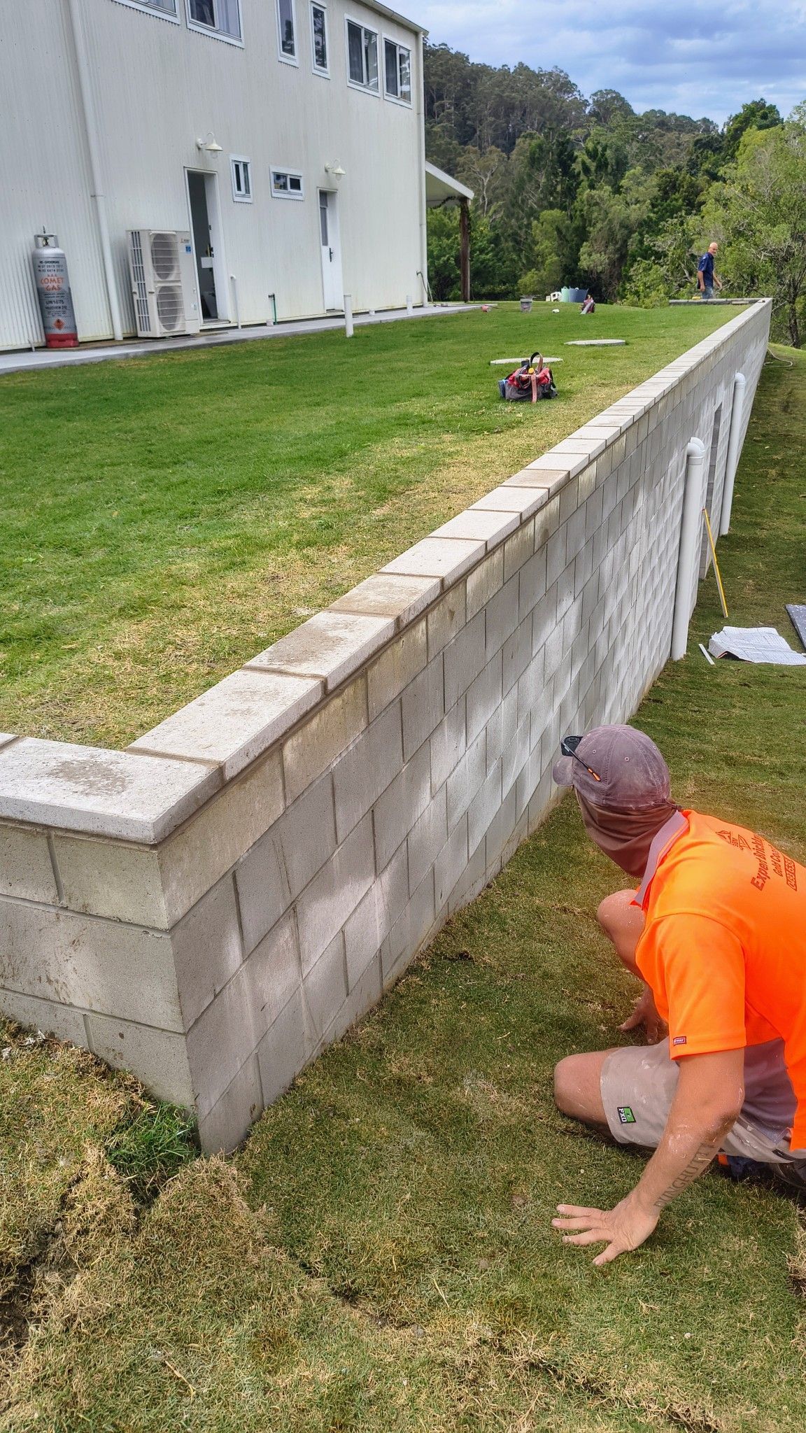 A Worker Installs Grass Near A Retaining Wall — Bricks By Dre In Oxenford, QLD
