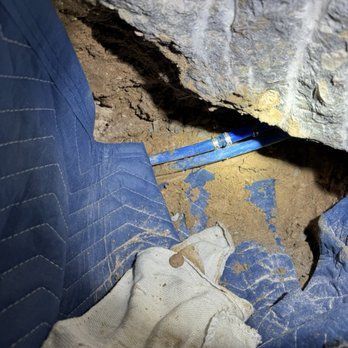 Blue pipes emerging from a rock wall; a blue moving blanket and dirty work glove are nearby.