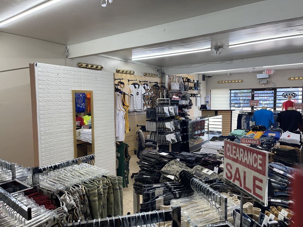 Clothing store interior, racks of clothing, clearance sale sign, overhead lighting.