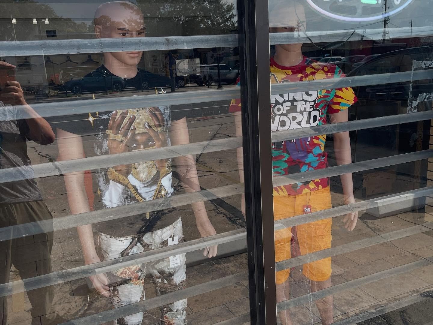 Three mannequins wearing clothes behind a window, reflecting the outside.
