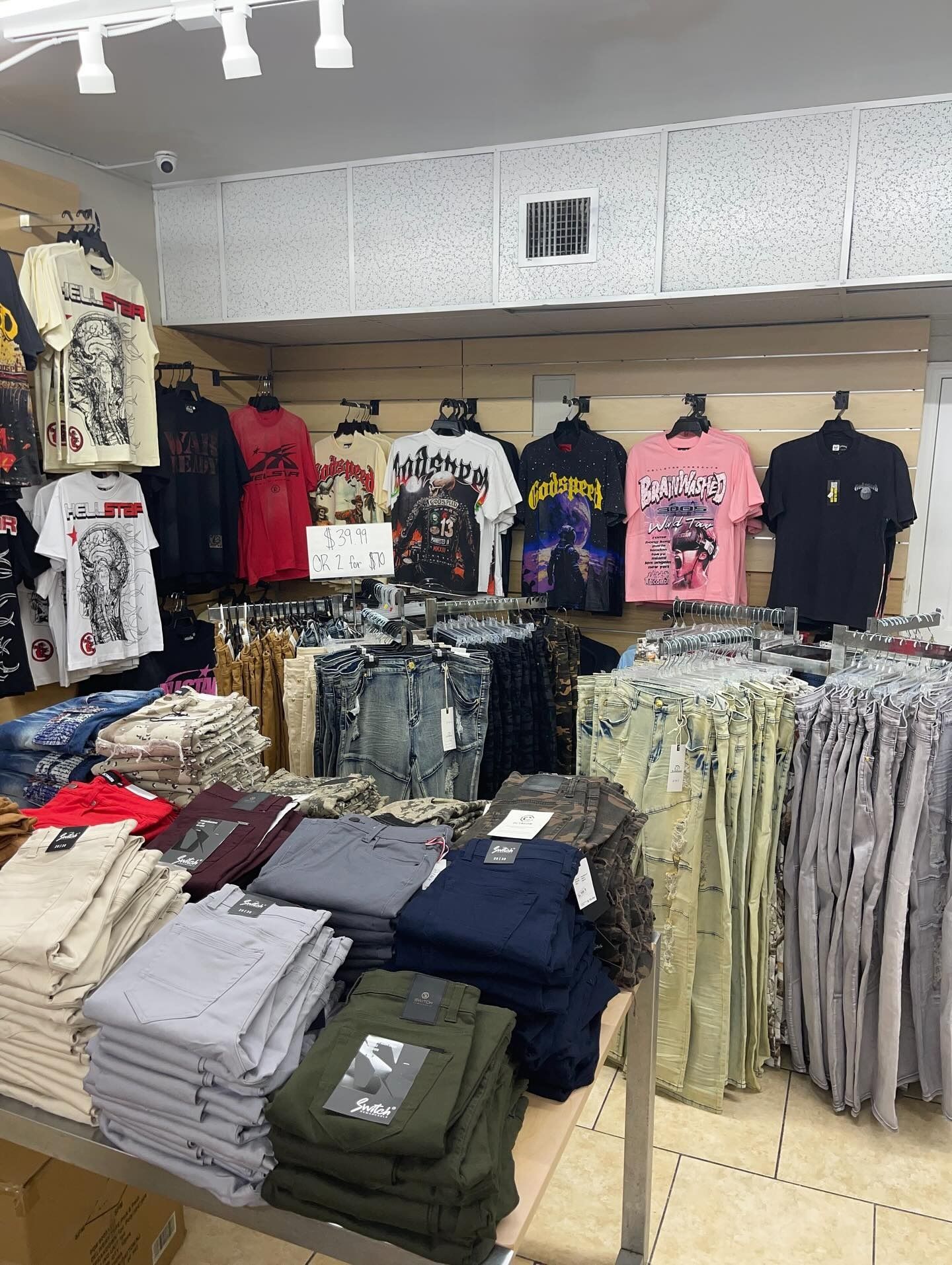 Clothing store interior with t-shirts hanging on display and folded pants on a table.