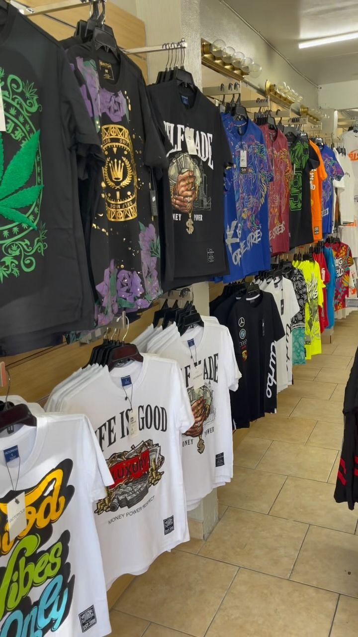 Row of graphic t-shirts hanging on display racks in a store. Variety of designs and colors, visible in an indoor setting.