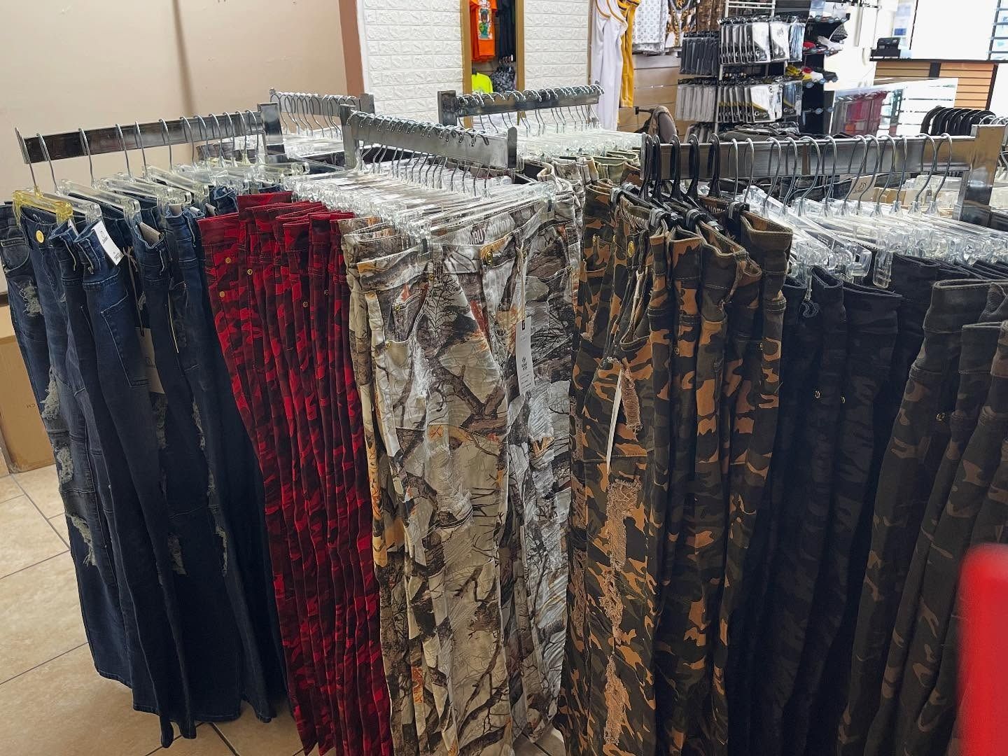 Clothing rack with various colored pants; denim, red, camouflage, and brown, in a store.