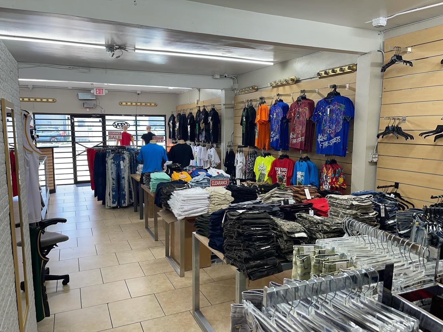 Clothing store interior with racks of clothing, some on hangers and some folded, in a bright setting.