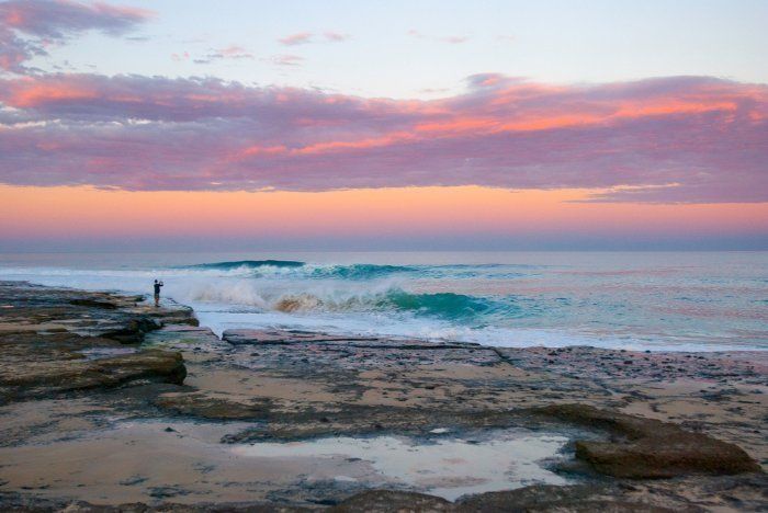 A Person Is Standing On A Pier Overlooking The Ocean At Sunset — Sal's Excavations In Ulladulla, NSW