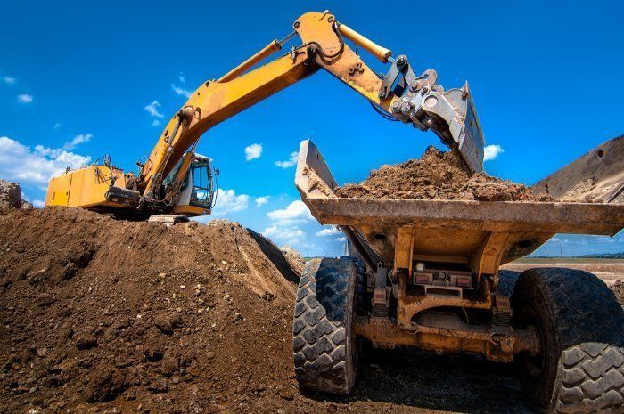 A Yellow Excavator Is Loading Dirt Into A Dump Truck — Sal's Excavations In Ulladulla, NSW
