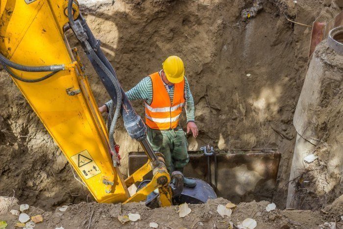 A Construction Worker Is Standing Next To A Yellow Excavator — Sal's Excavations In Falls Creek, NSW