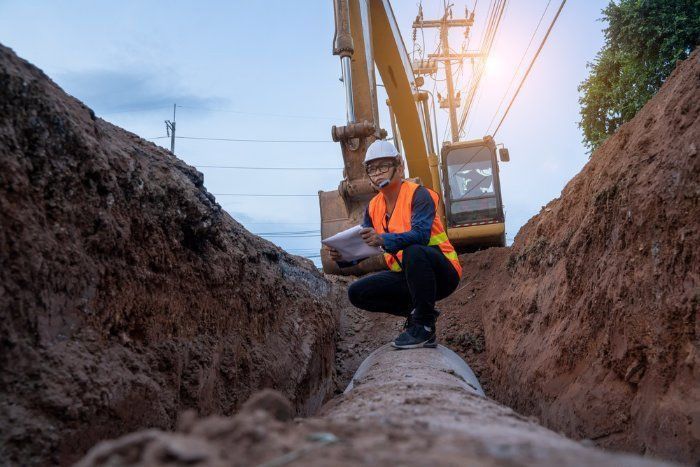A Construction Worker Is Kneeling Down In A Trench Looking At A Clipboard — Sal's Excavations In Falls Creek, NSW