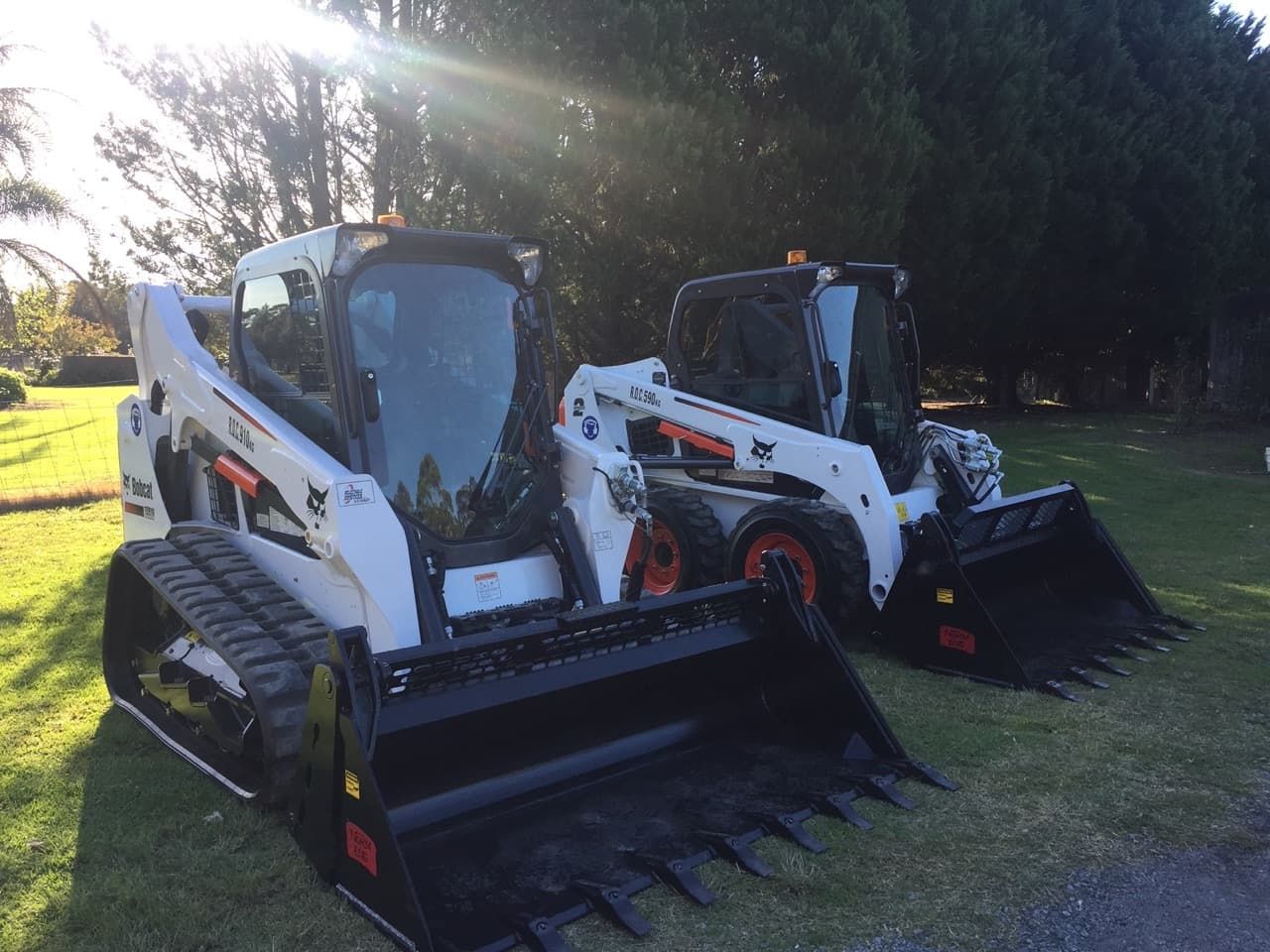 Two Bobcat Tractors Parked Next To Each Other In A Grassy Field — Sal's Excavations In Nowra, NSW