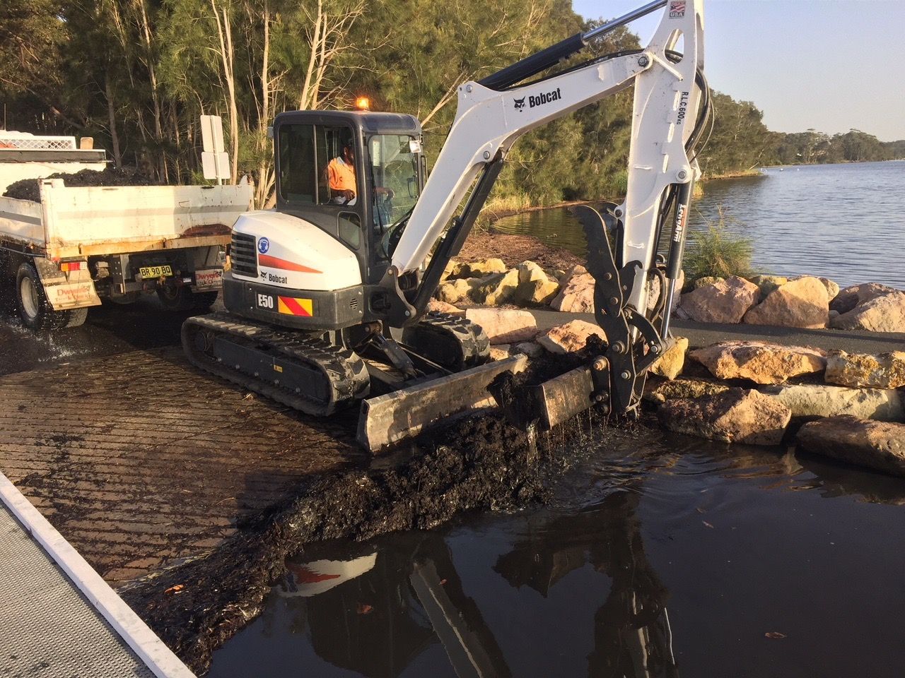 A Small Excavator Digging Waste In The Water — Sal's Excavations In Falls Creek, NSW