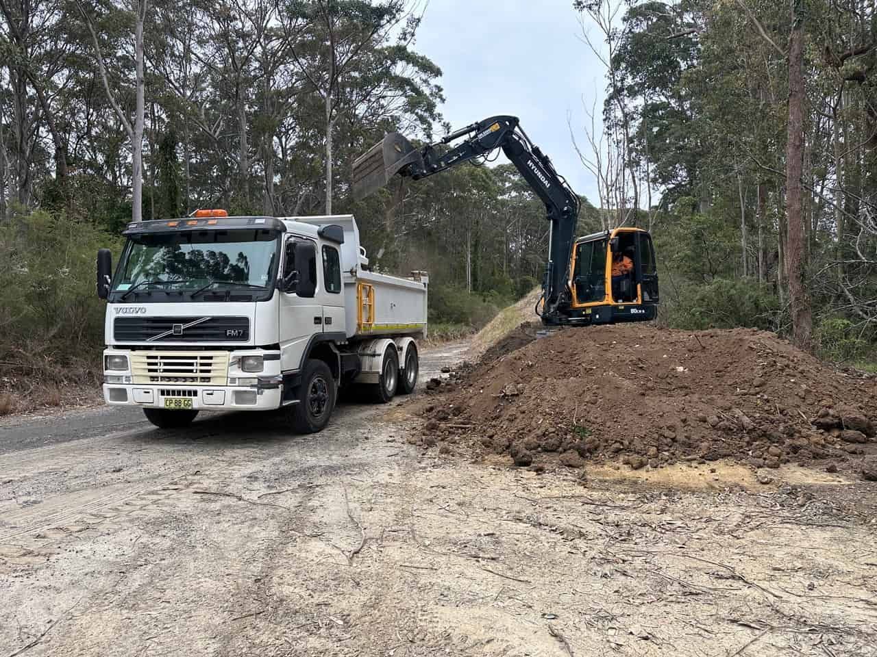 A Dump Truck Driving Down A Dirt Road Next To An Excavator — Sal's Excavations In Falls Creek, NSW