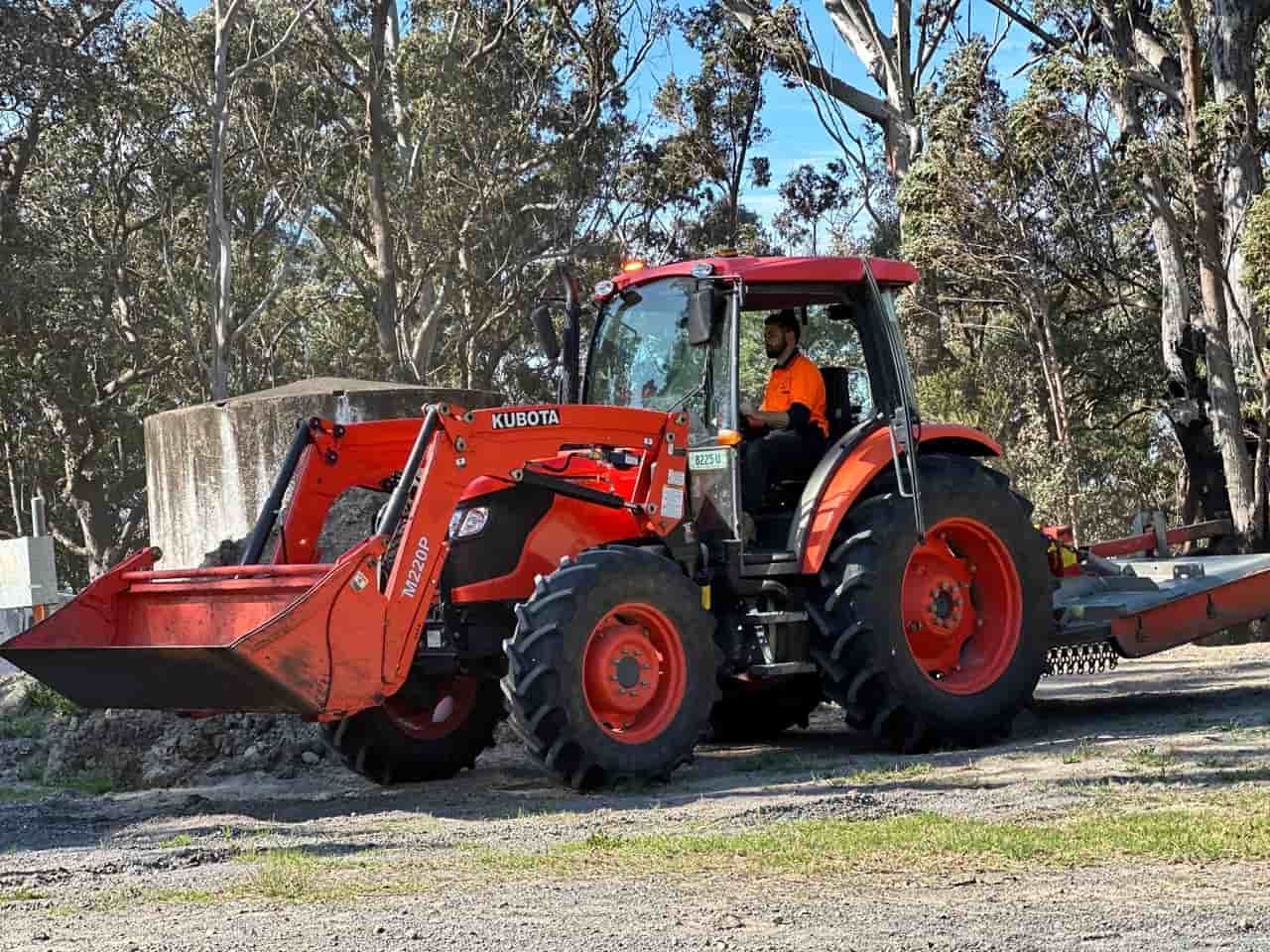 A Man Driving A Red Tractor With A Bucket Attached To It — Sal's Excavations In Vincentia, NSW