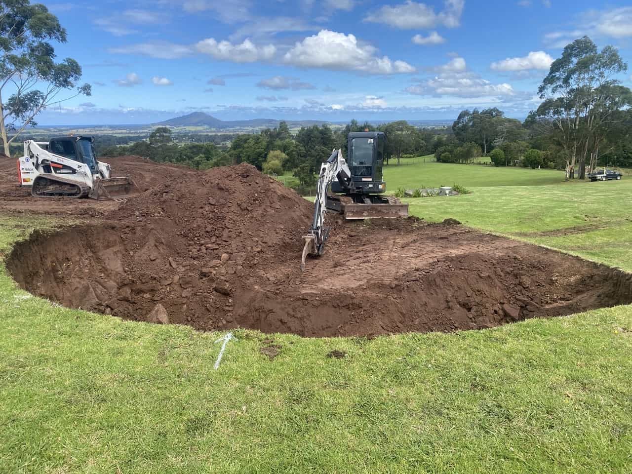 A Bulldozer Digging A Hole In The Ground In A Grassy Field — Sal's Excavations In Vincentia, NSW