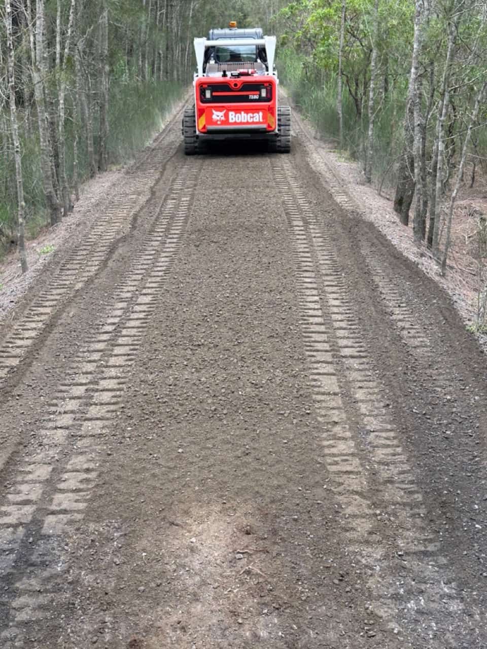 A Bobcat Tractor Driving Down A Dirt Road — Sal's Excavations In Vincentia, NSW