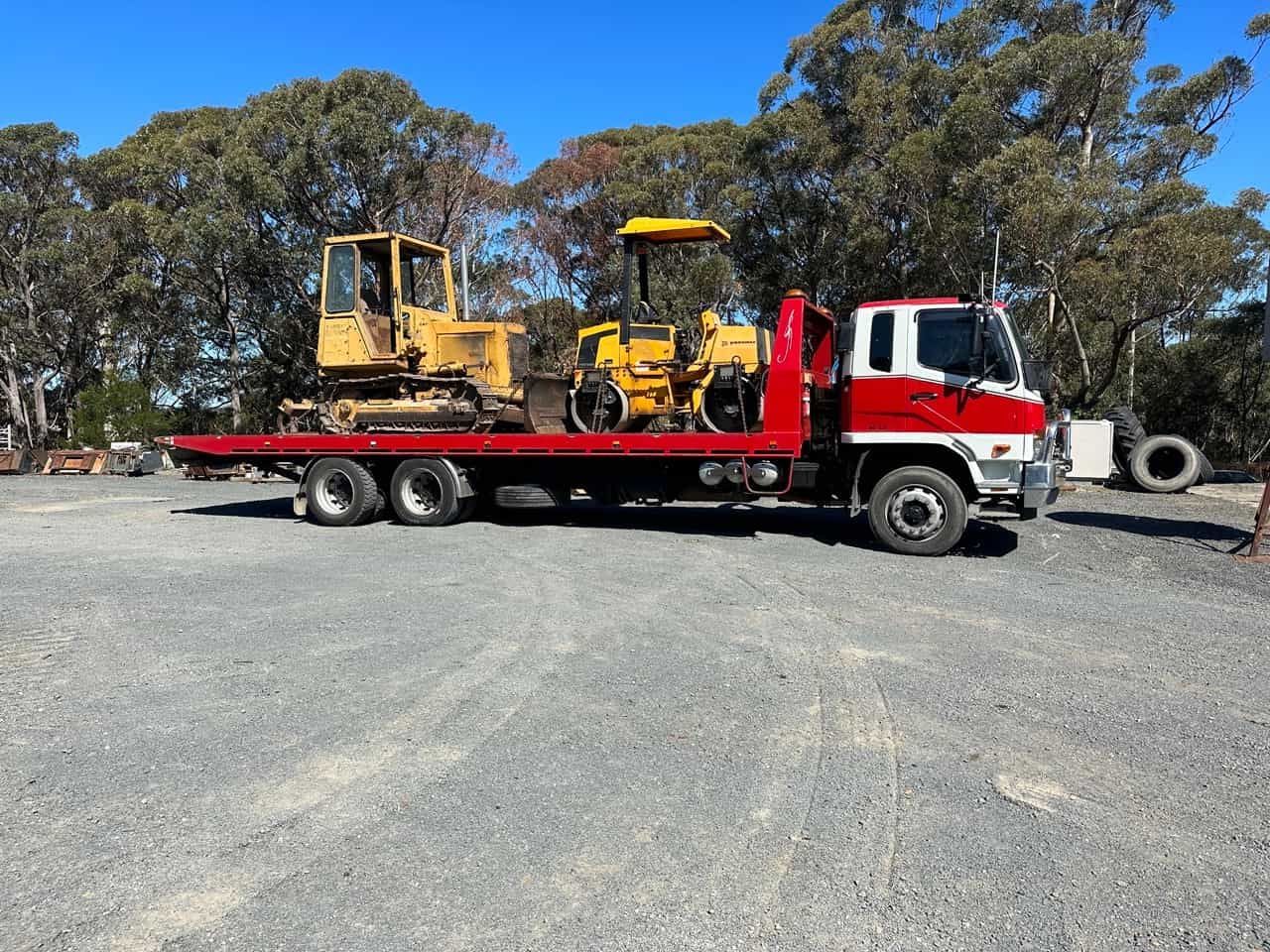 A Red Tow Truck With A Yellow Bulldozer On The Back Of It — Sal's Excavations In Vincentia, NSW