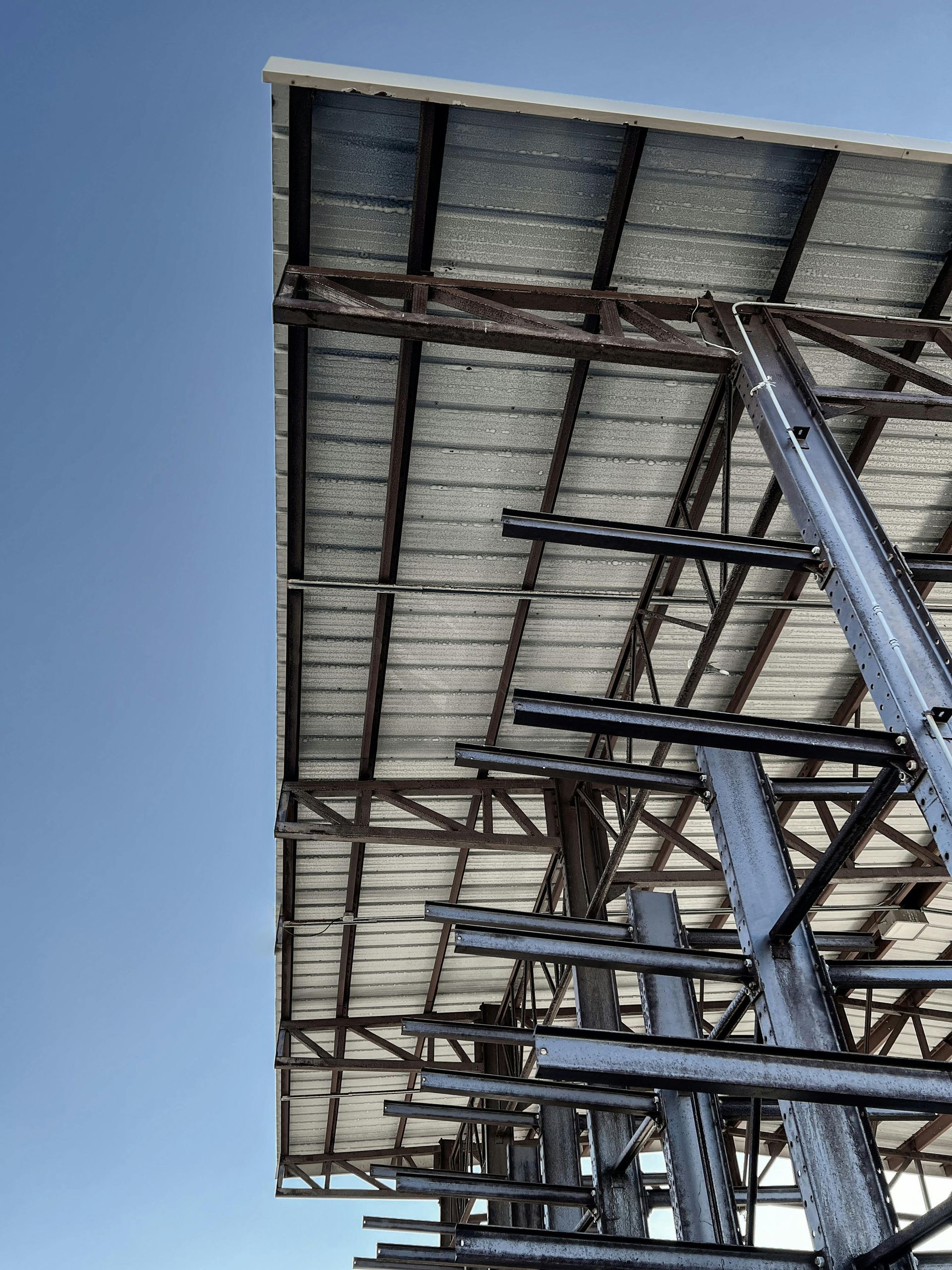 Steel roof structure viewed from below against a clear blue sky