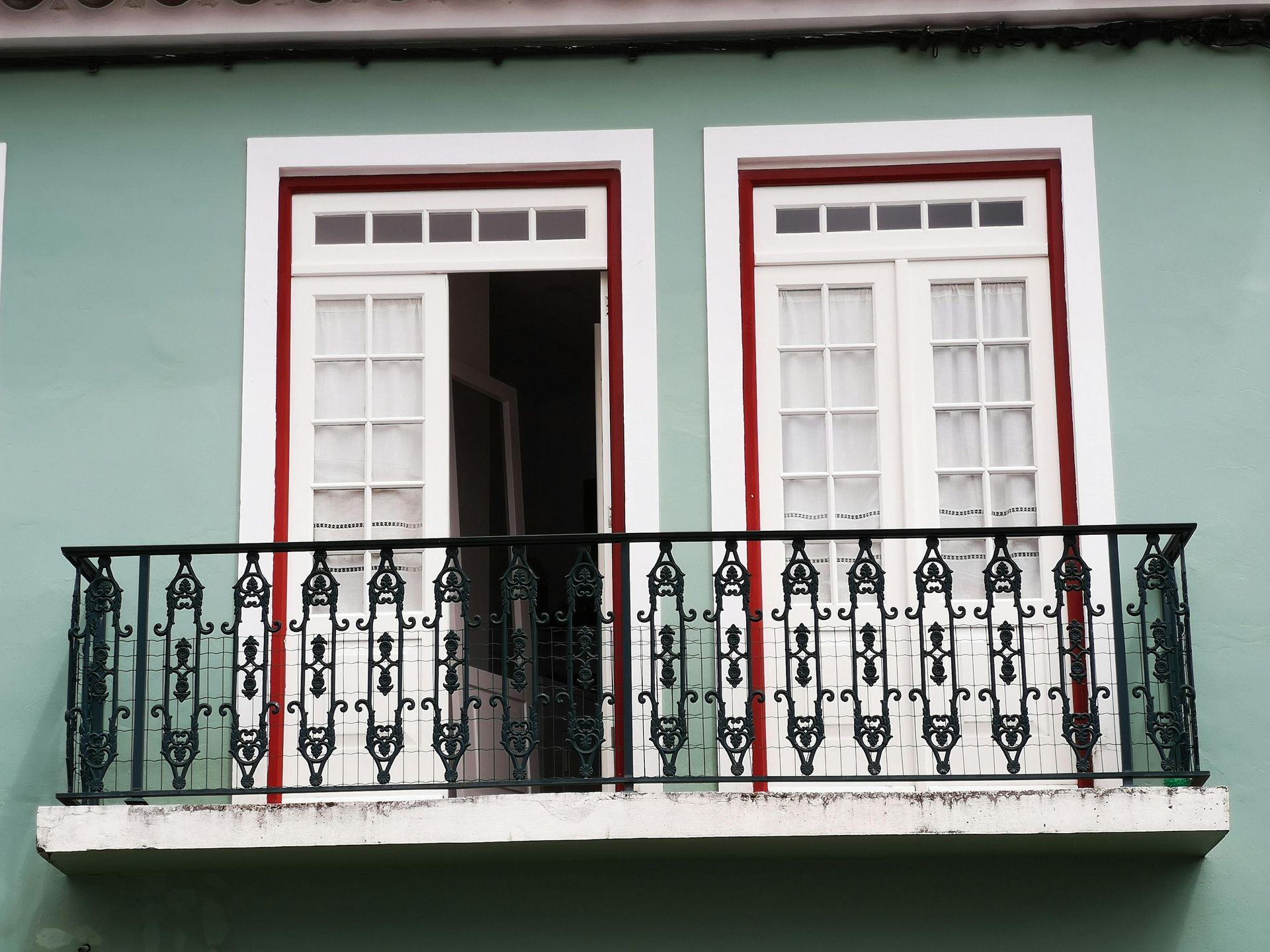 Balcony with black wrought-iron railing and white French doors on a mint-green building facade