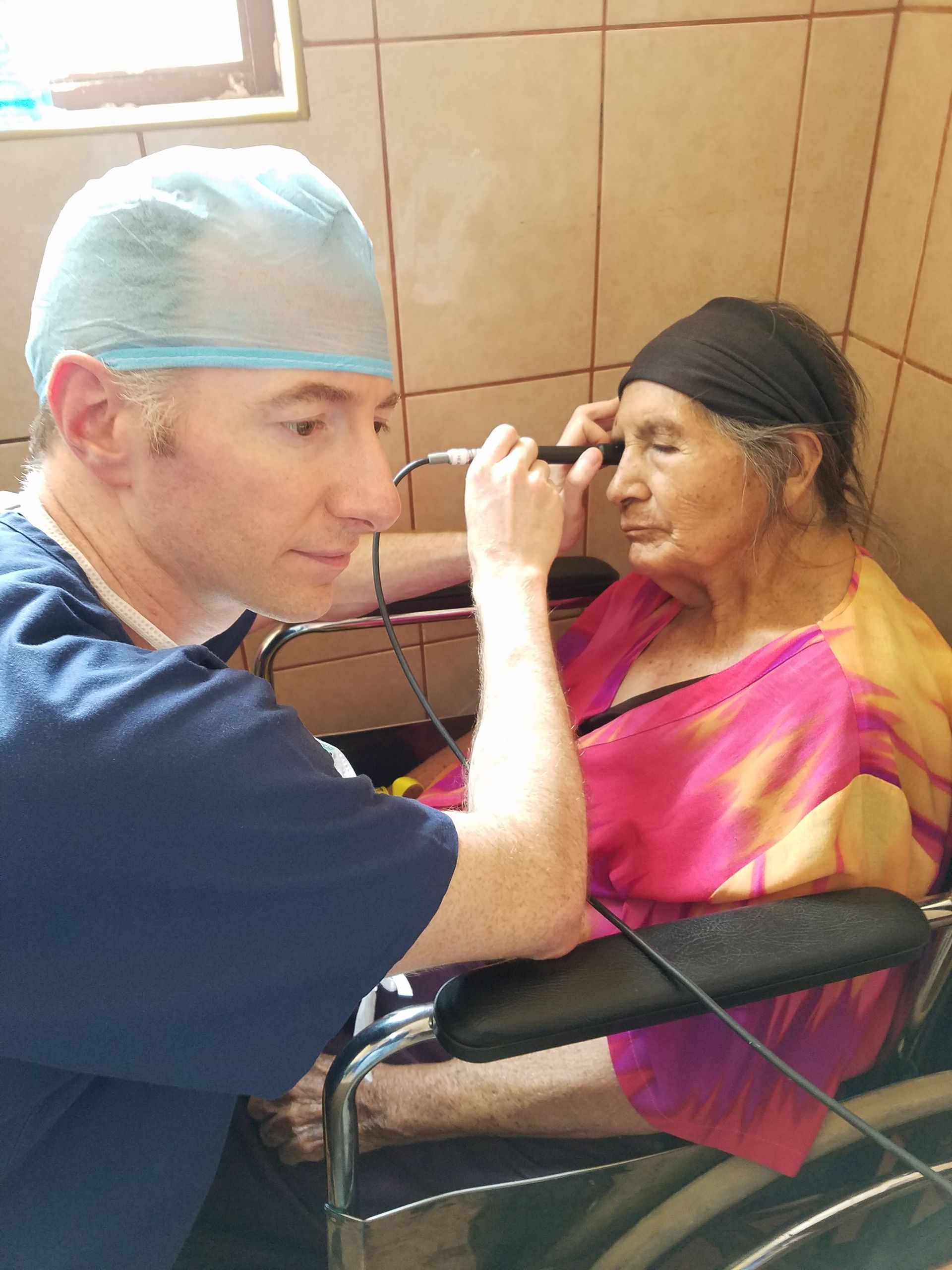 A man is applying makeup to an elderly woman in a wheelchair