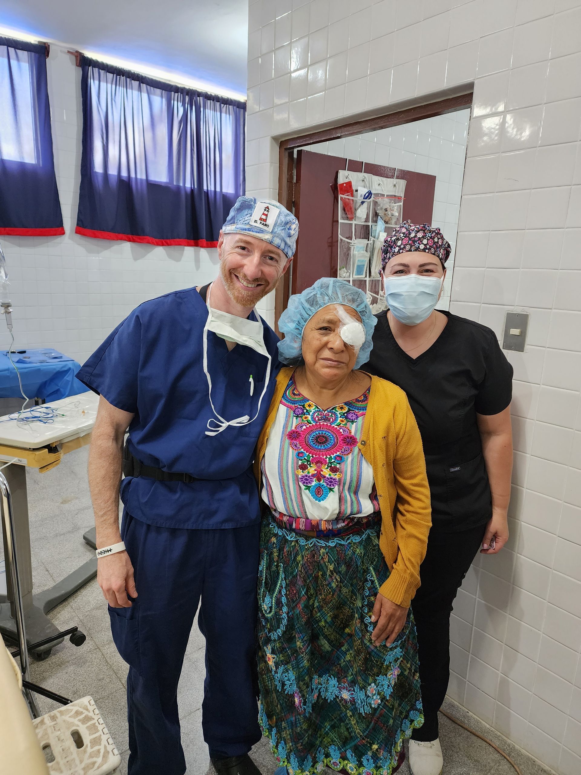 A surgeon and two nurses are posing for a picture with a patient in an operating room.