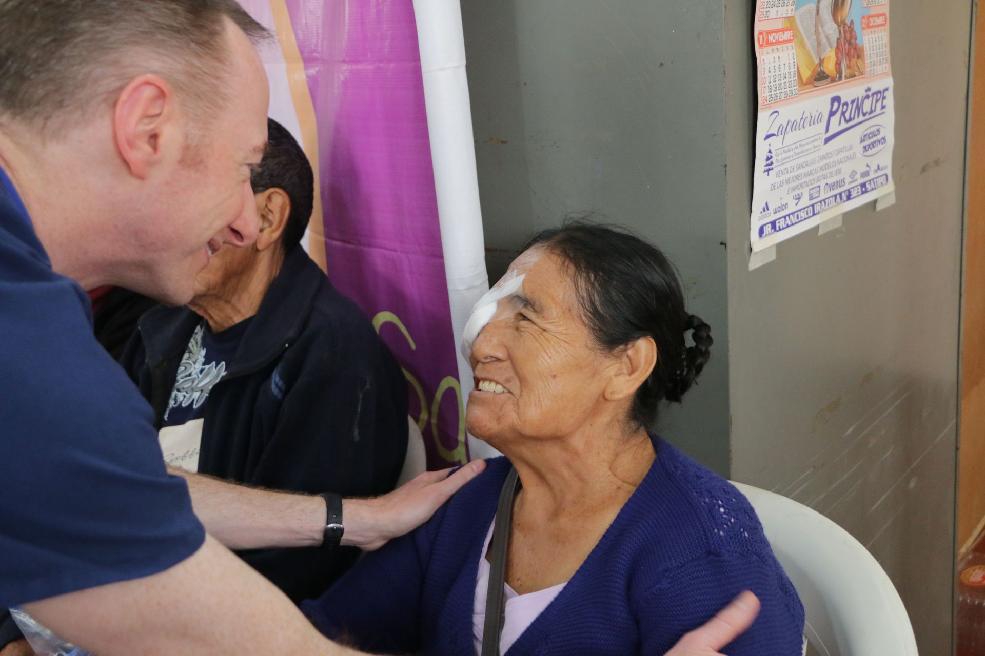A man is putting a bandage on an older woman 's eye