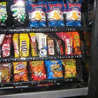 A vending machine filled with a variety of snacks including fritos and skittles