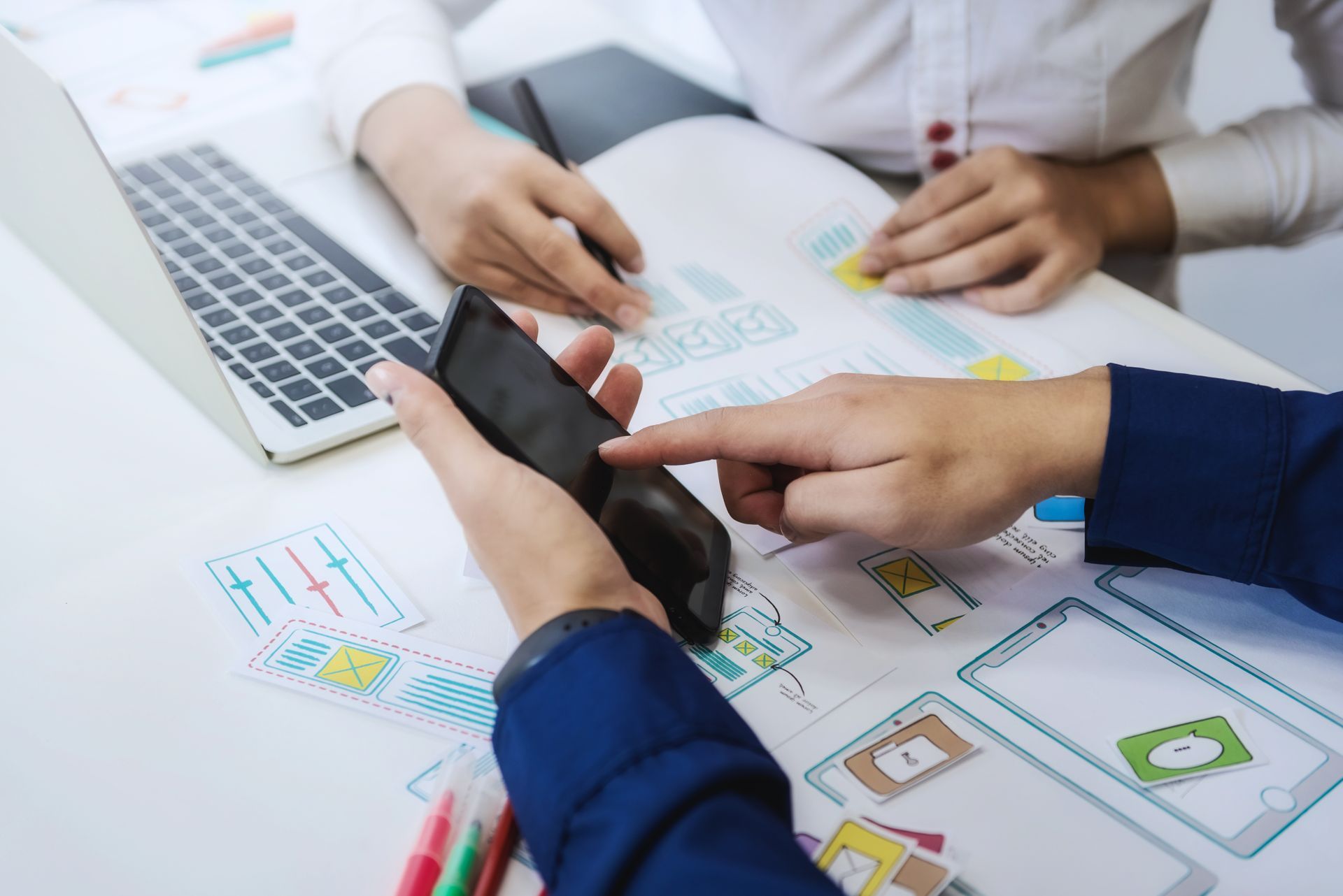 A group of people are sitting at a table looking at a cell phone.