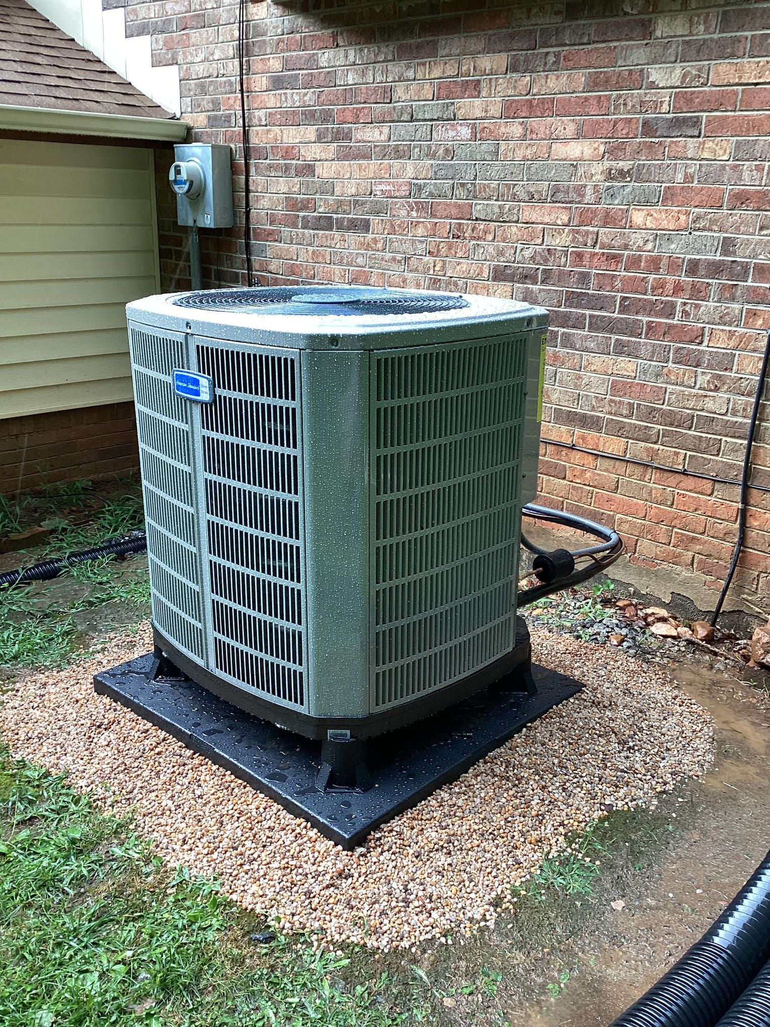 A large air conditioner is sitting on top of a pile of gravel in front of a brick building.