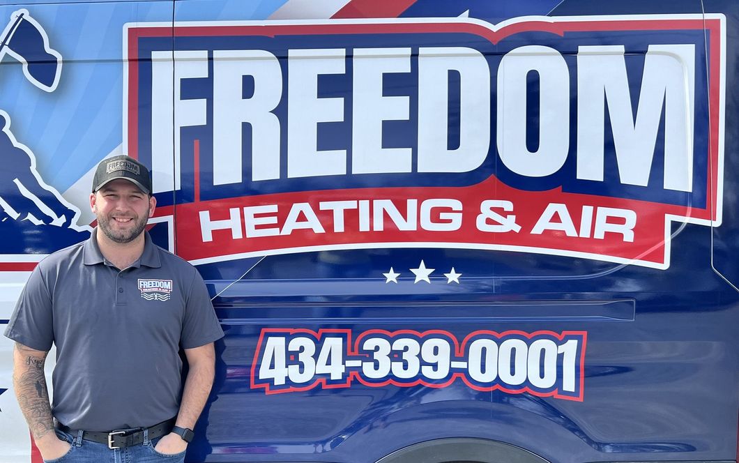 A man is standing in front of a freedom heating and air truck.