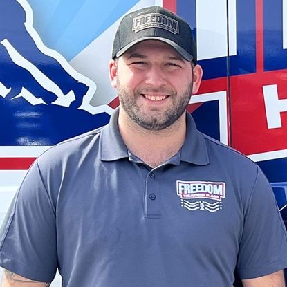 A man wearing a hat and a freedom shirt is standing in front of a van.