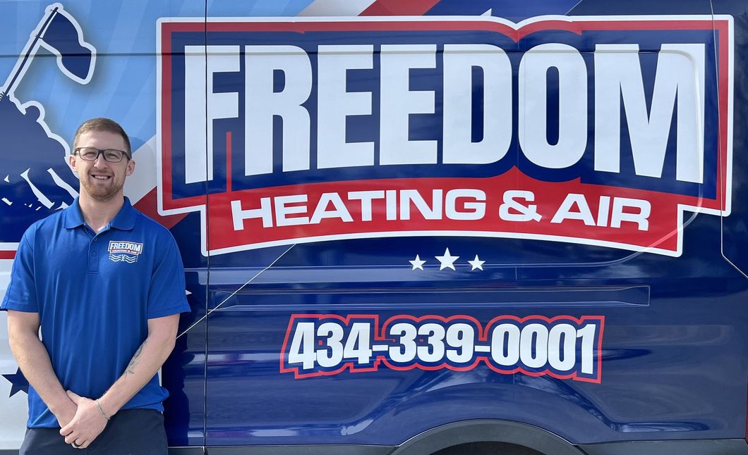 A man is standing in front of a freedom heating and air truck.