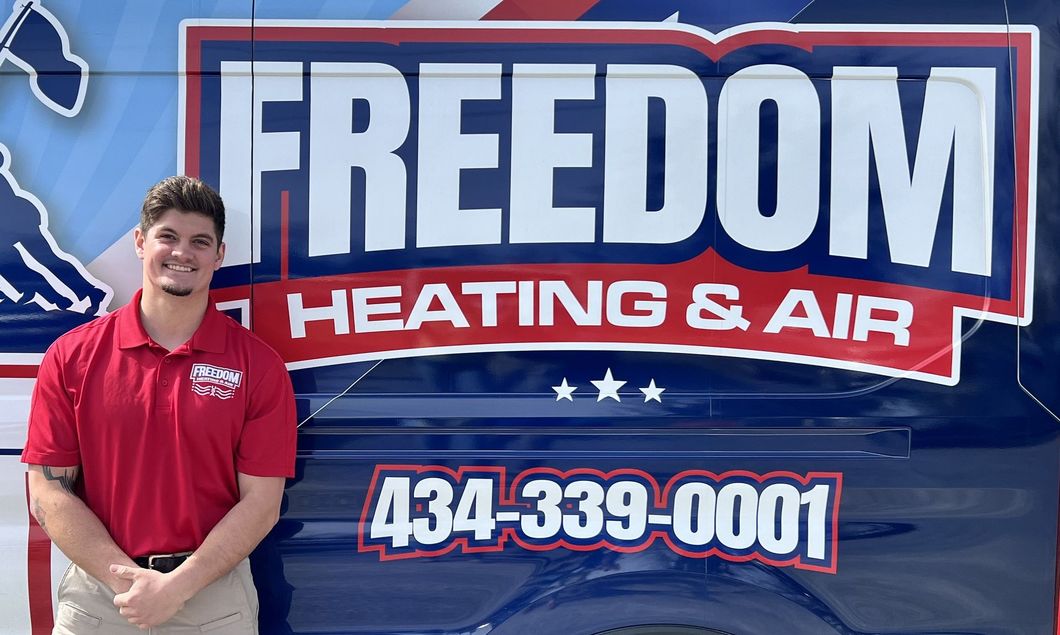 A man in a red shirt is standing in front of a freedom heating and air van.