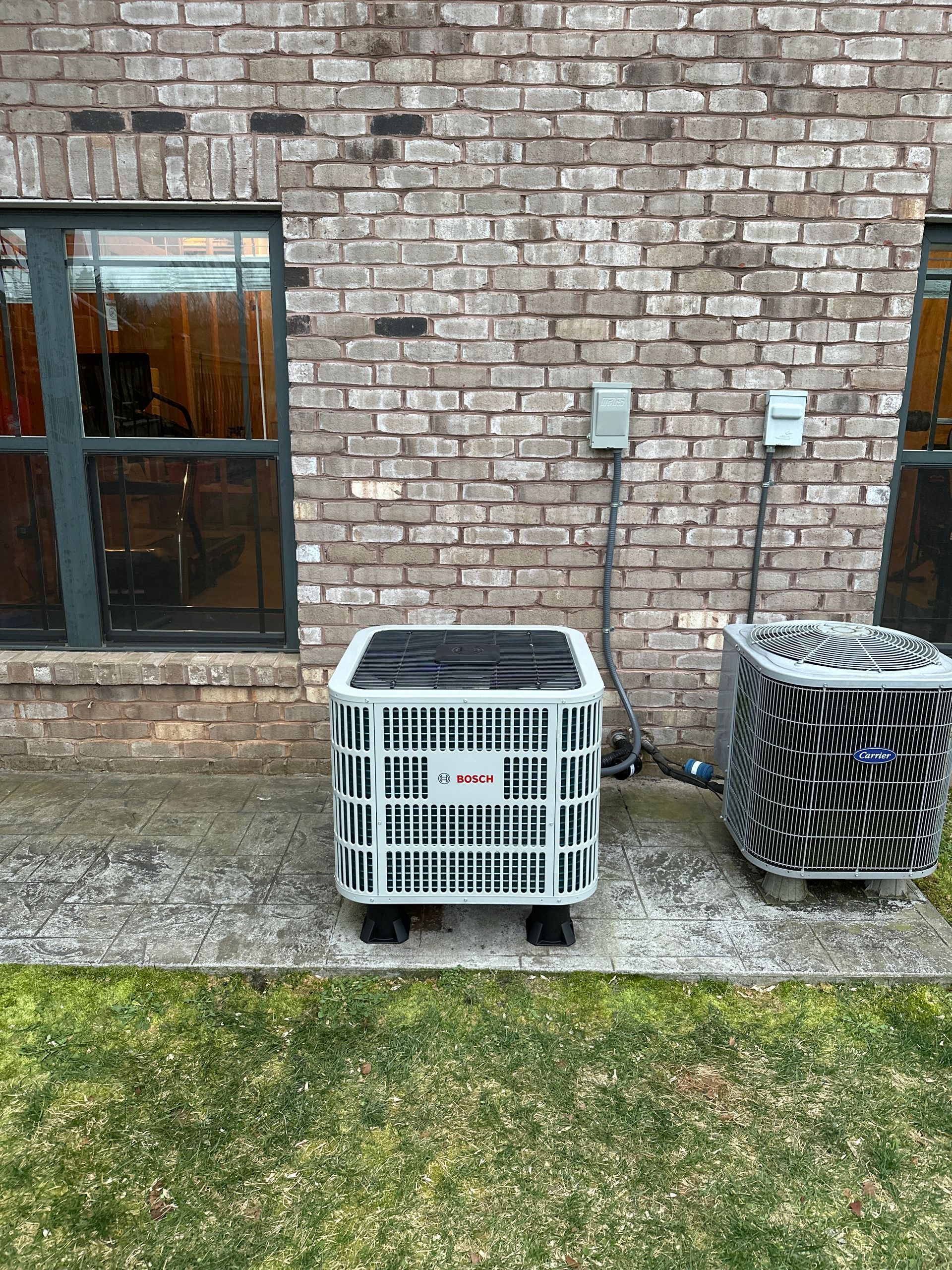 Two air conditioners are sitting in front of a brick building.