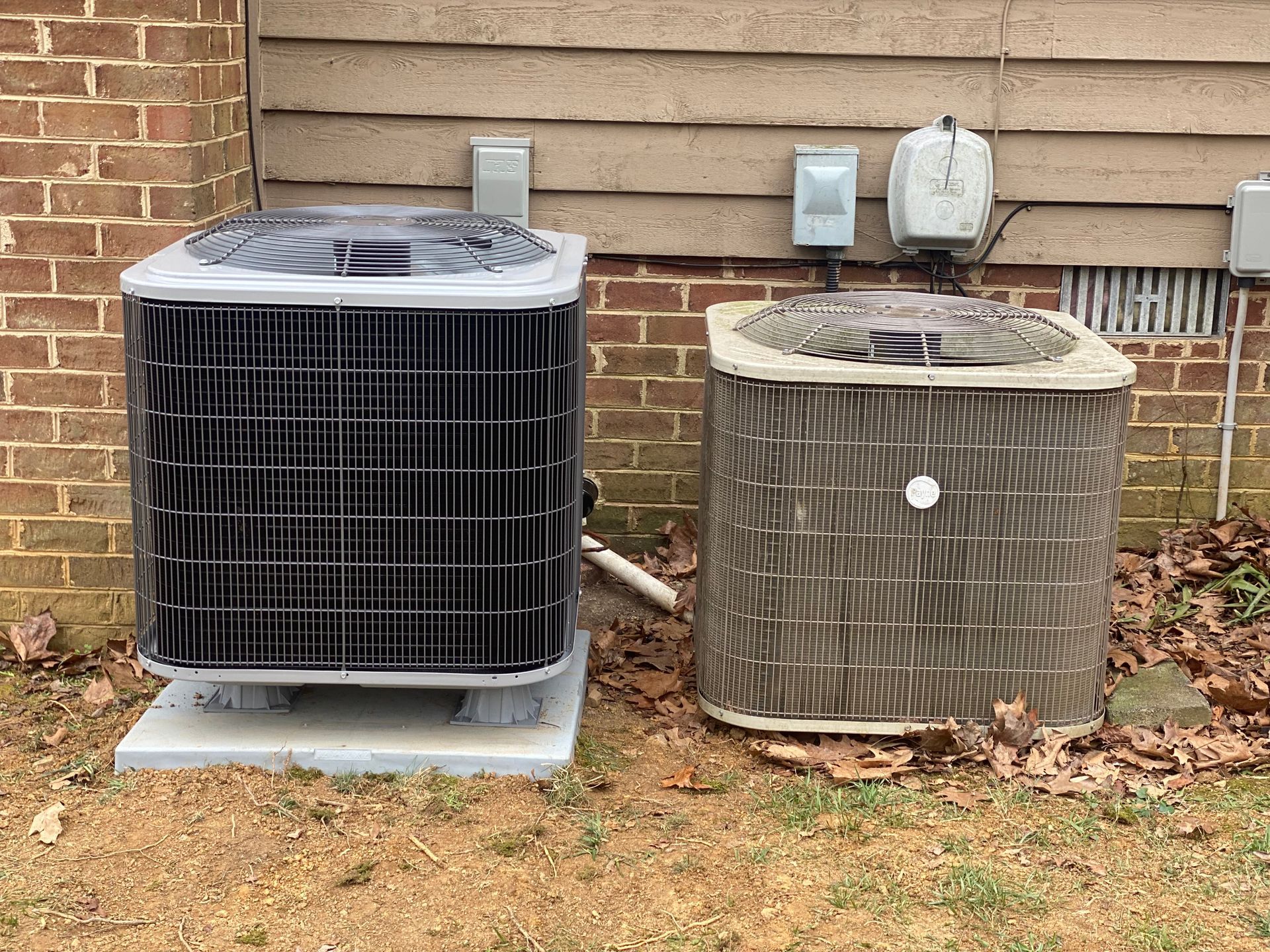 Two air conditioners are sitting next to each other in front of a brick building.