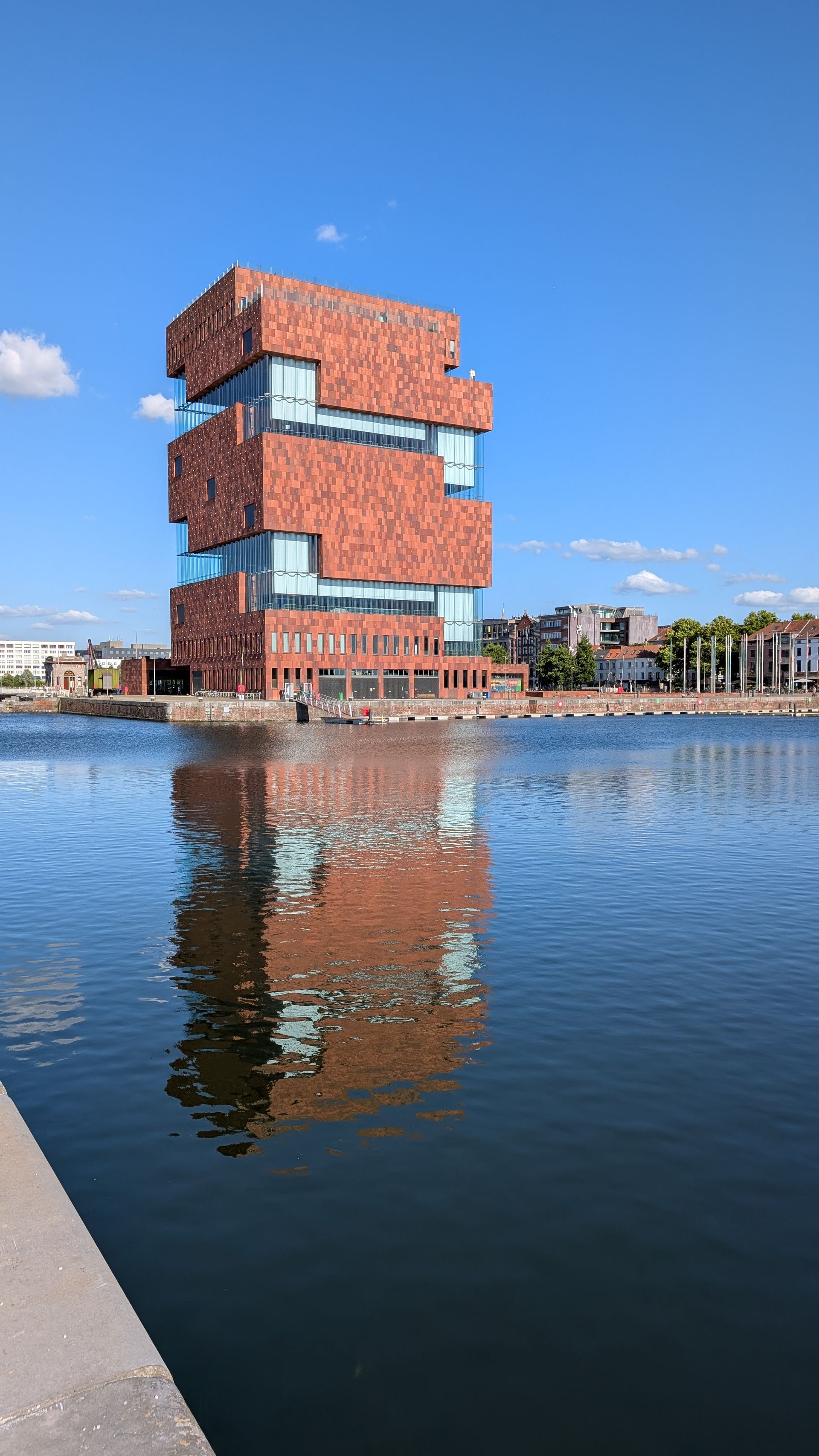 Brick-clad museum building reflected in water, against a blue sky. Antwerp, Belgium.