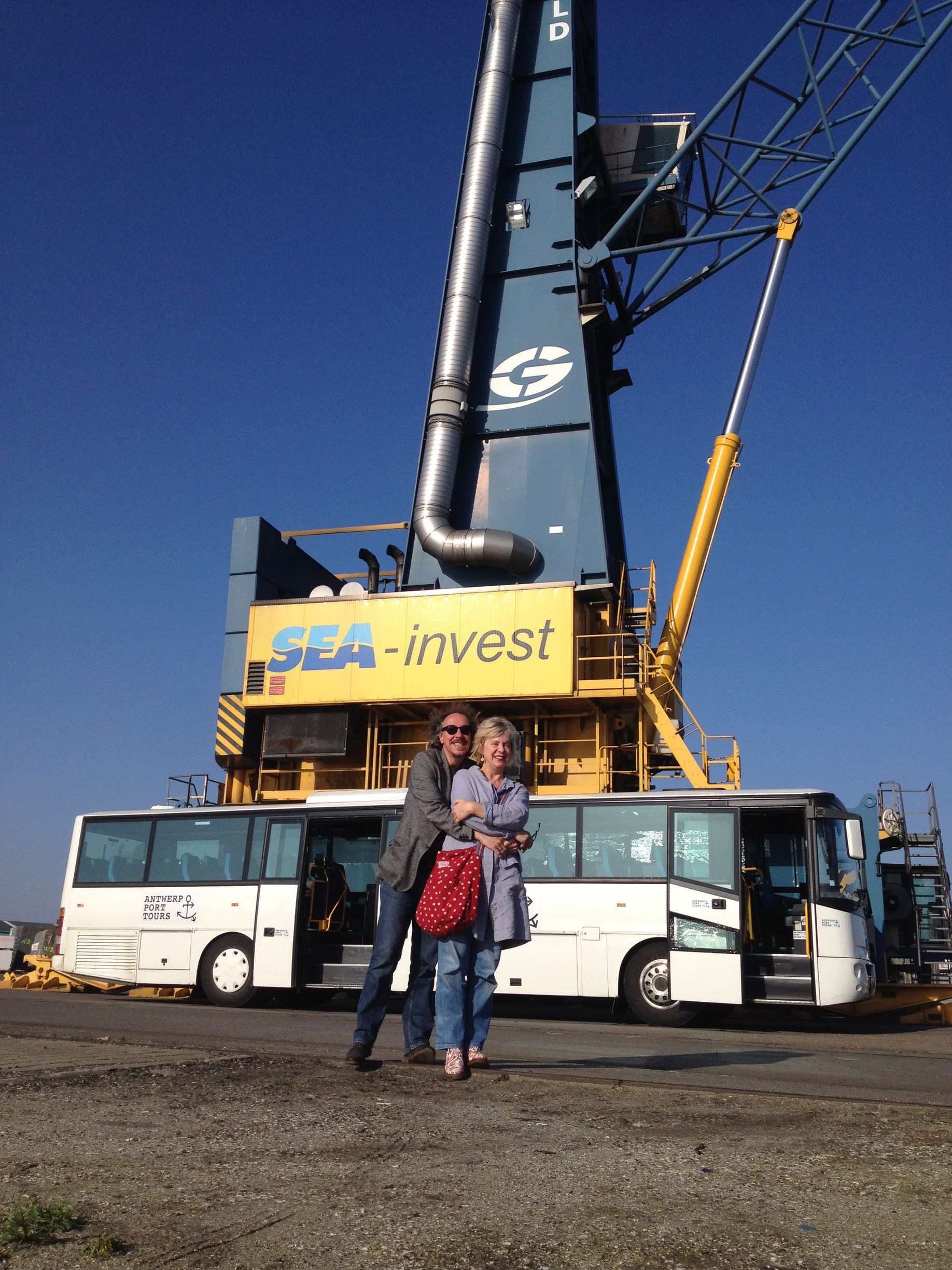 Couple embraces in front of a bus and large blue crane at 