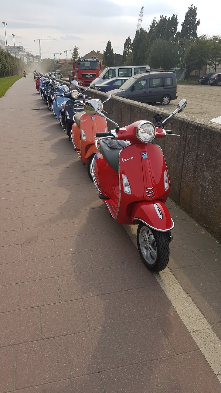 Line of colorful scooters parked next to a low stone wall, red scooter in the foreground.