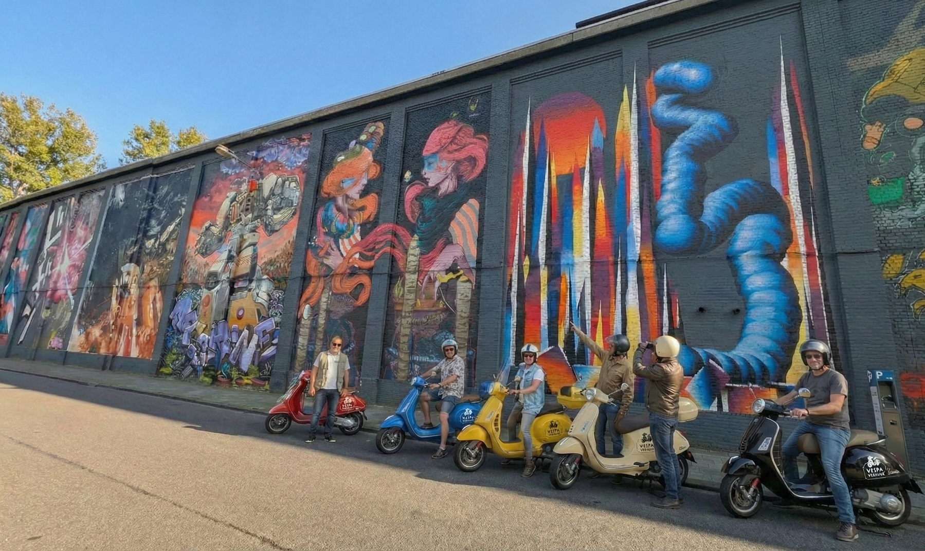 Man taking selfie with group of people on scooters in front of cargo ship at dock.