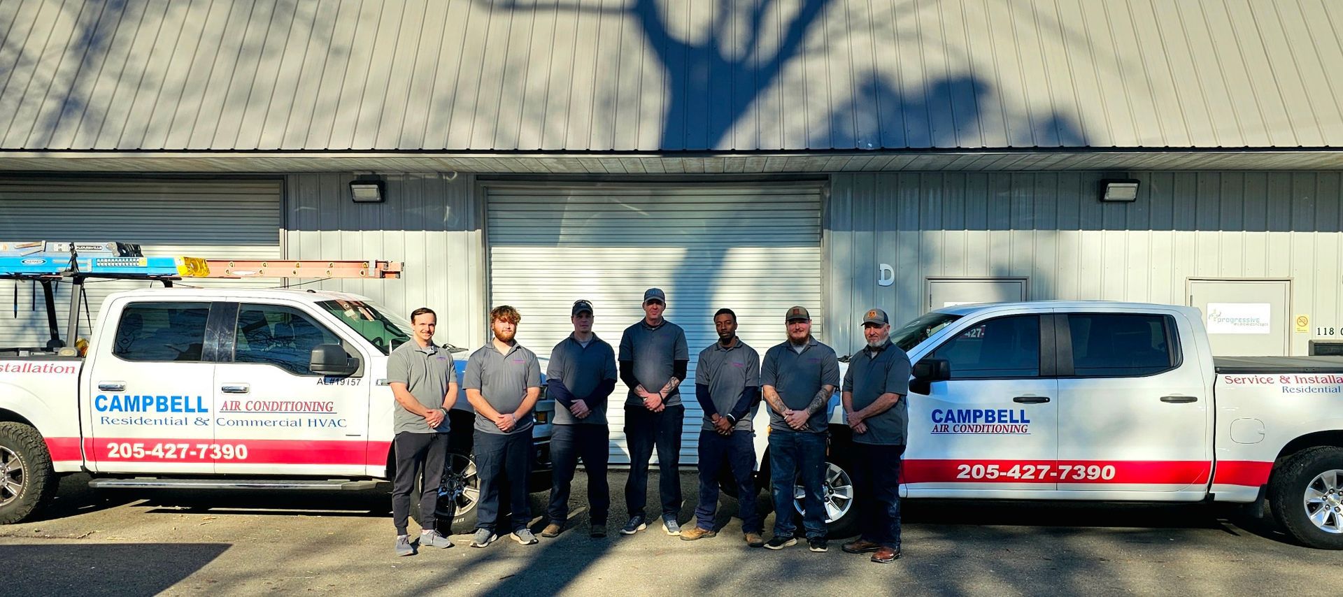 Group of workers pose with company trucks in front of a building.