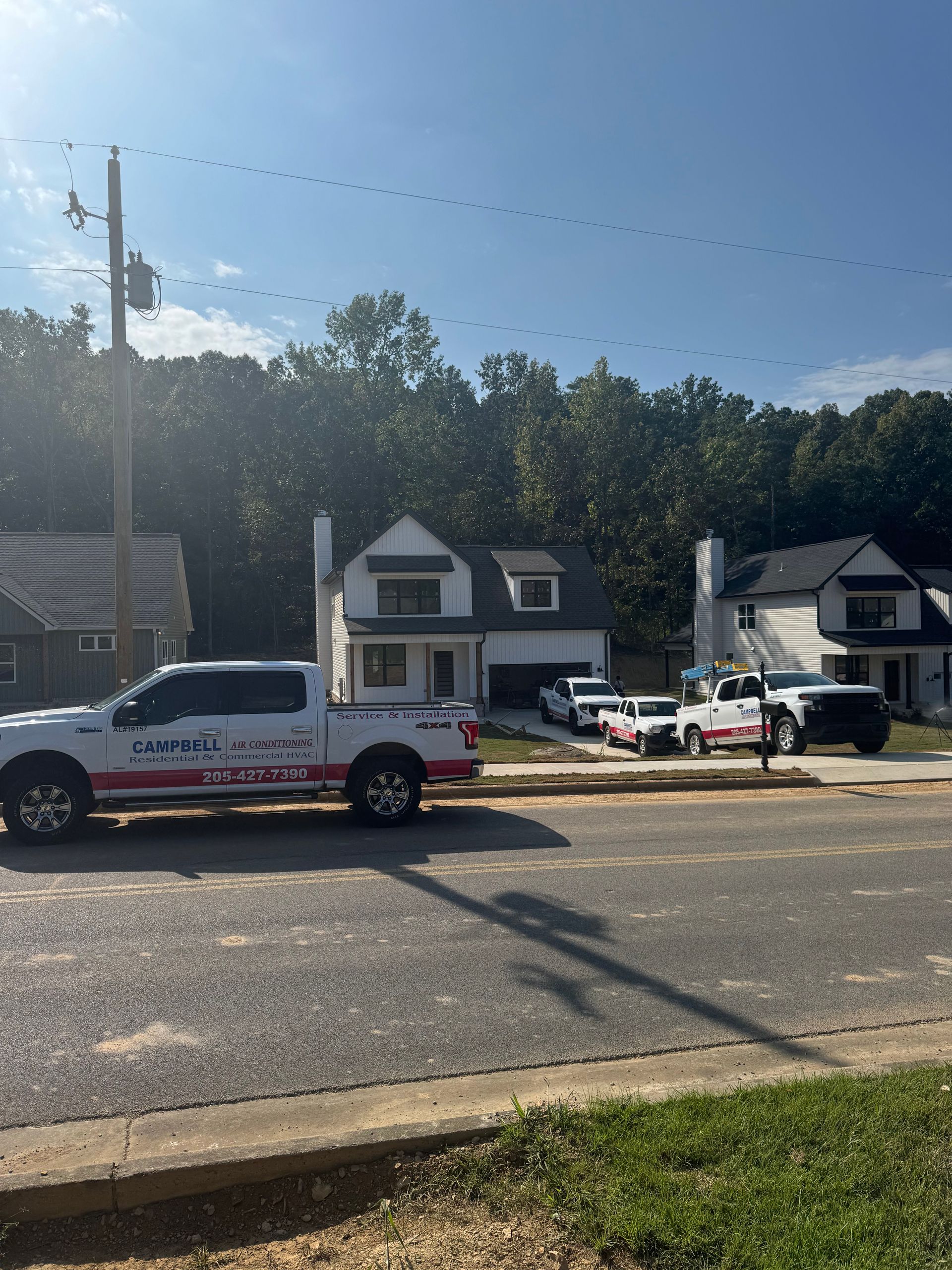 White trucks parked in front of modern houses. A power pole and trees are in the background. Sunny day.
