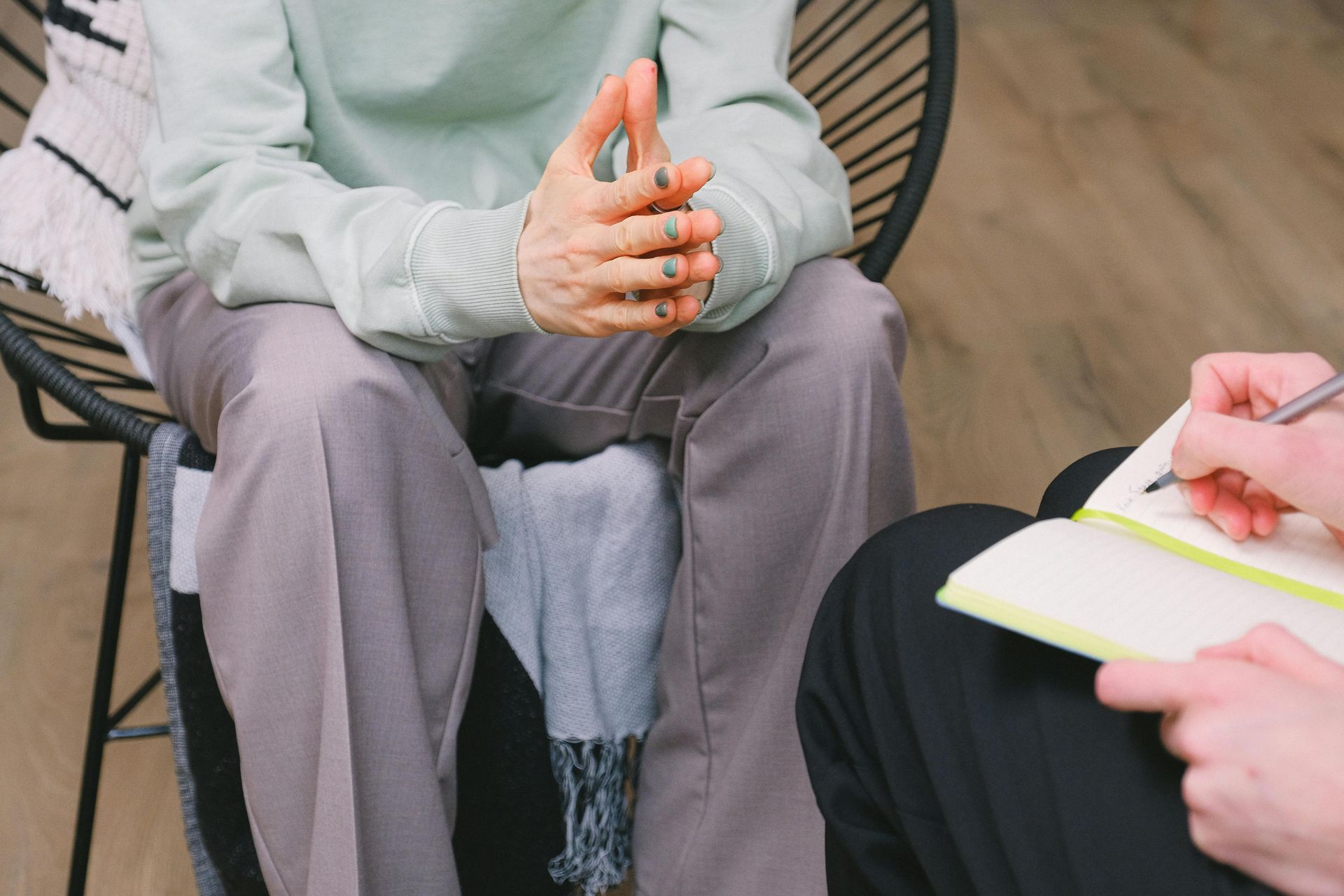 A woman is sitting in a chair talking to a man who is writing in a notebook.