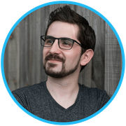 a picture of Jon from Jon Web Design with glasses and a beard is standing in front of a wooden wall .